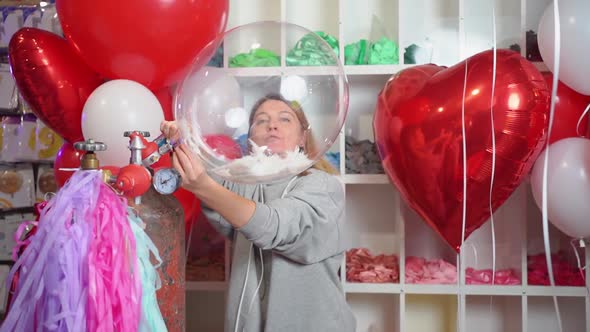 Woman Inflates with Helium a Transparent Balloon with White Feathers Inside