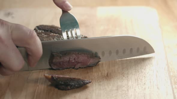 Slow motion Slider shot of medium Rare Beef Steak Being Sliced With chefs Knife and Fork on a Wooden