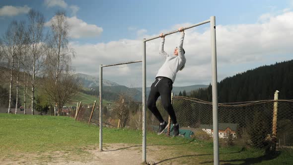 Man pulling up on horizontal bar while training in city park outdoors