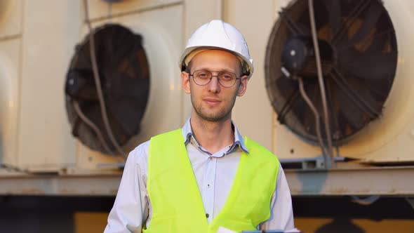 Portrait of smiling engineer in helmet making diagnosis of an industrial air conditioning