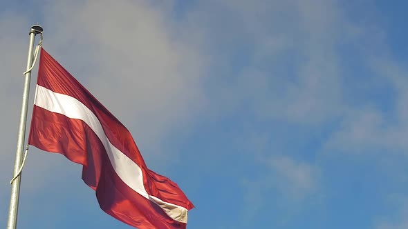 Large Latvian flag in sunny day with blue sky, slow motion