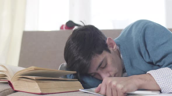 Close-up Portrait of Young Caucasian Boy Sleeping on Couch with Book and Tablet. Exhausted Male