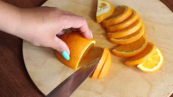 Closeup Girl Cuts a Ripe Juicy Orange on a Wooden Board