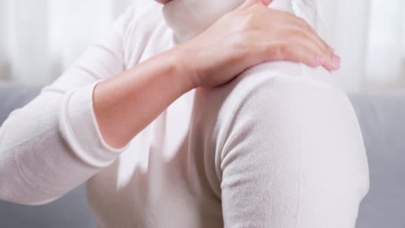 Close up of woman sitting on sofa doing self massage on shoulder and arm for relieving pain and gett