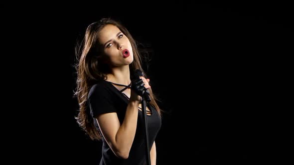 Girl in a Microphone Sings Driving Songs and Smiles. Black Background