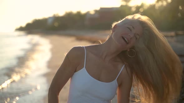 Slow motion of backlit mature woman on a beach shaking her hair to the right and smiling at the came