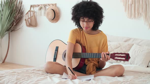 Afro American Girl Learning to Play the Guitar By Writing Chords on a Sheet of Paper
