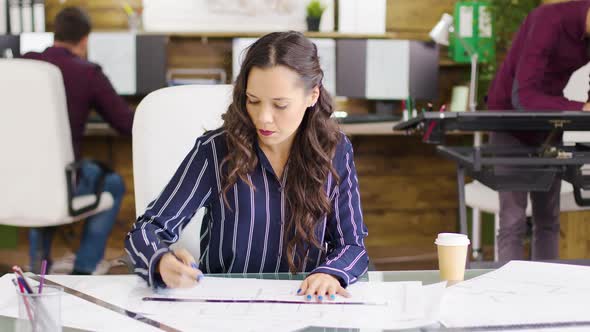 Young Female Architect Taking a Sip of Coffee While Working on Blueprints