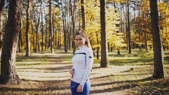 Young Woman Smiling Listening to Music Through Earphones Connected to Mobile Phone Posing in Autumn