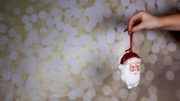 A woman's hand with gold glittery nails holding a Santa ornament with a glittery background