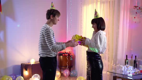 Side View of Happy Smiling Man Giving Gift Box To Birthday Woman Lady Shaking Present Returning It