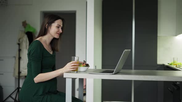 Pregnant Woman Sitting and Eats Salad While Having a Video Call on Laptop at Home