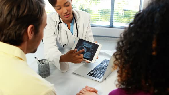 Female doctor with digital tablet showing ultrasound scan of baby to couple