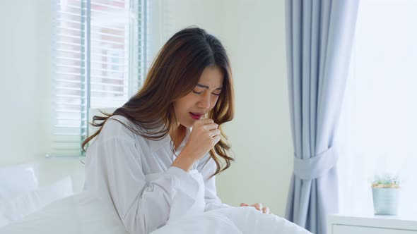 Attractive young woman feeling bad after wake up on bed and coughing in early morning at home.