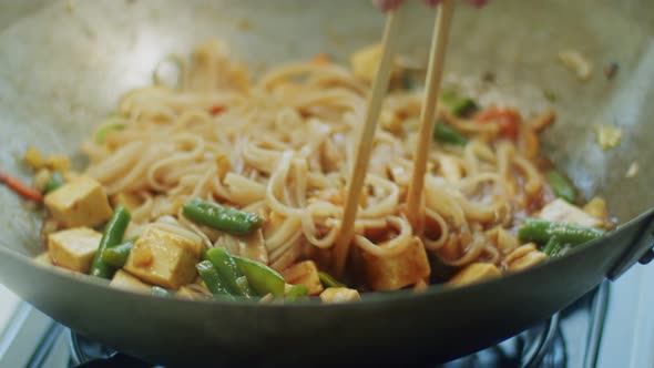 Woman mixing delicious wok noodles with chopsticks