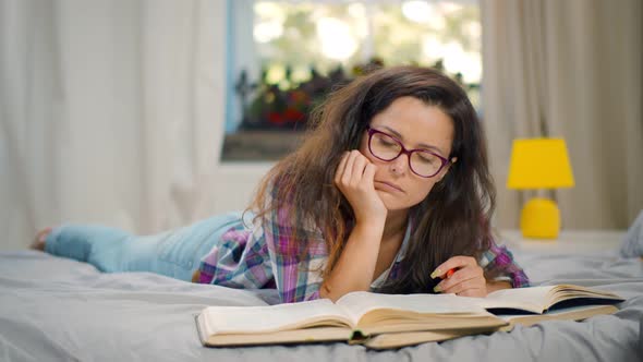 Tired Female Student Falling Asleep Doing Homework on Bed