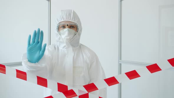 Portrait of Woman in Medical Protective Uniform Stretching Arm Forbidding Entrance in Quarantine