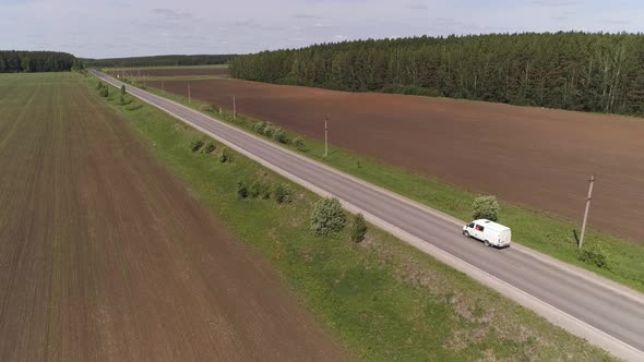 Aerial view of white commercial vehicle driving on a straight asphalt road