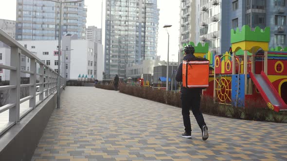 Delivery Man with Backpack Walking Past Buildings