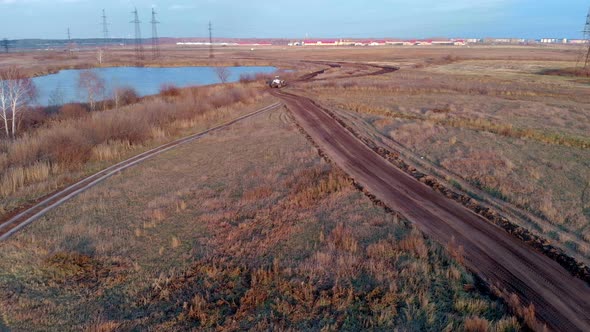 The Drone Flies Behind a Tractor By a Grader That Levels a Country Road Among the Fields