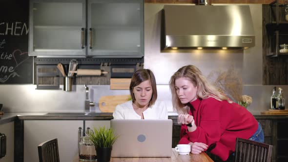 Women discuss a work project on a computer in the kitchen of the house