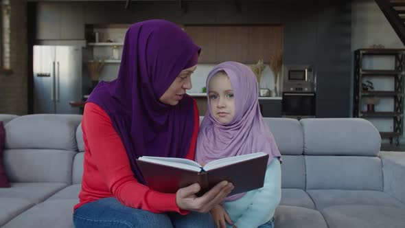 Loving Charming Muslim Mother and Cute Little Girl Reading Book Together at Home