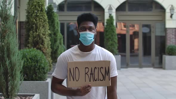 Young African American Man a Medical Mask Holding Carton Poster with Writing Slogan NO RACISM