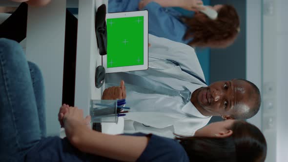 Vertical Video Tripod Shot of Pediatrician Showing Horizontal Green Screen on Tablet