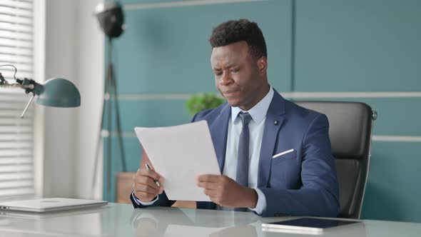 African Businessman Upset While Reading Documents in Office