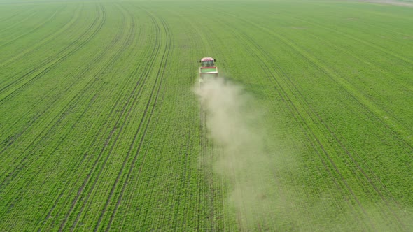 A red tractor against a background of a green field sprays mineral fertilizers.