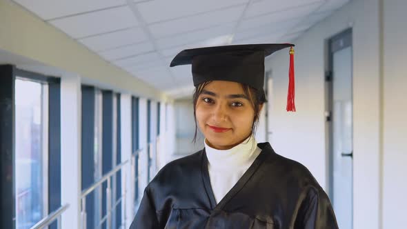 Indian Female Graduate in Mantle Stands with a Diploma in Her Hands and Smiles