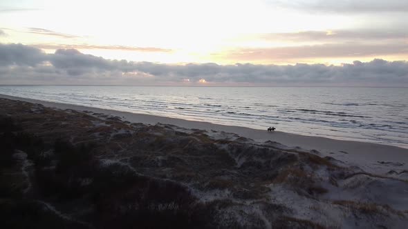 Aerial drone flyover Perkone sandy beach Baltic sea coastline, two horse riders at the beach after t