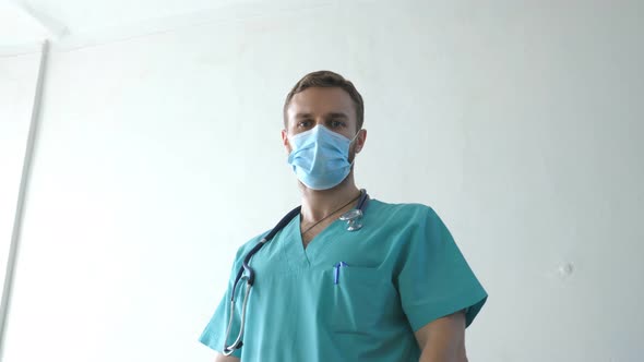 Portrait of Young Male Caucasian Doctor with Medical Face Mask Looks at Camera alt