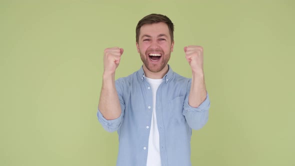 Handsome Young Man Rejoices Raising His Arms Feeling Victory Close Up on Green Background