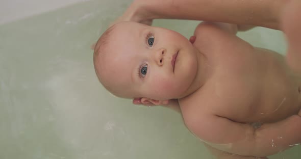 Calm Infant Lying in a Bath and Looking Up with Smile While Mother Washing Him
