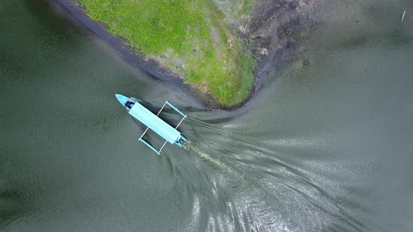 Aerial footage of a blue motor boat travelling down a narrow lake.