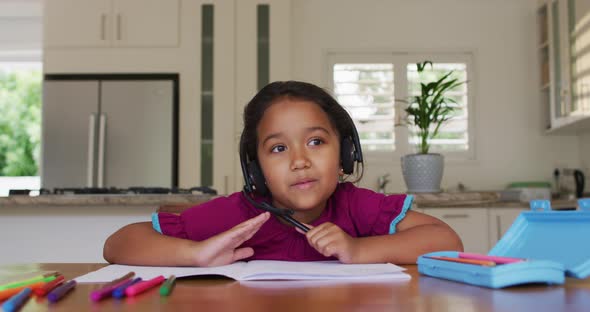 Hispanic girl sitting at table having video call wearing headset