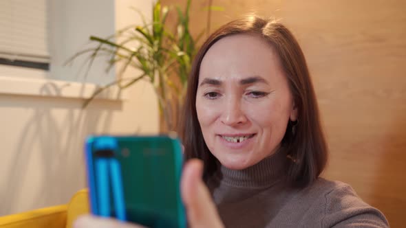 Happy Woman Sits in a Chair and Chats on Social Networks Using Mobile Phone Smartphone