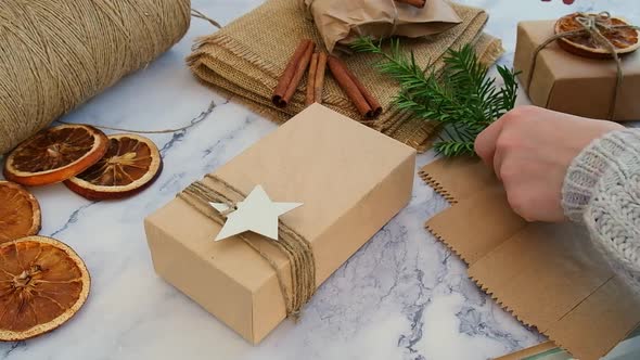 Woman Making Box with New Year's Gifts Wrapped in Craft Paper and Decorated with Fir Branch