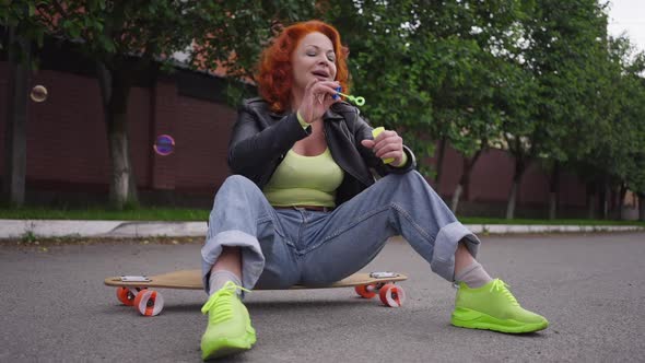 Wide Shot Relaxed Retro Woman Sitting on Vintage Skateboard Outdoors Blowing Soap Bubbles in Slow