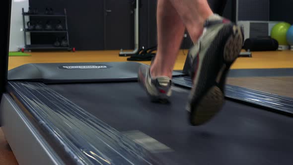 A Fit Man Jogs on a Treadmill in a Gym - Closeup on the Feet From Behind