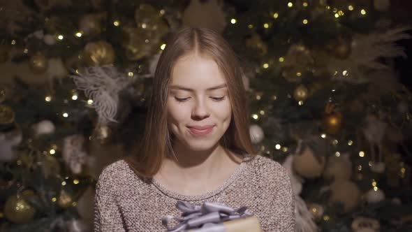 Cute Young Girl Gives a Christmas Present, Against the Background of the Christmas Tree. Slow Motion