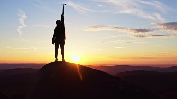 Aerial View of a Silhouette of a Woman Standing on the Top of a Mountain Happily Waving Her Hands