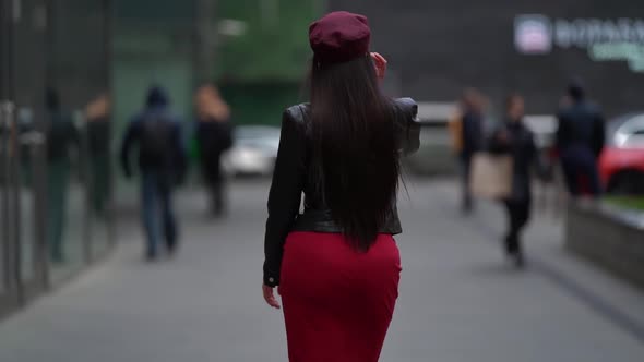 a Brunette with Long Hair in a Black Leather Jacket a Red Skirt and a Burgundy Cap Walks Away