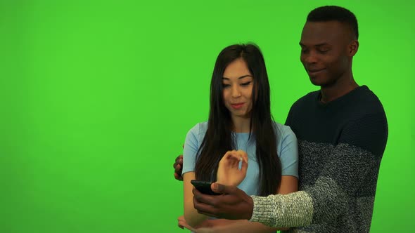 A Young Black Man and a Young Asian Woman Work at the Smartphone - Green Screen Studio