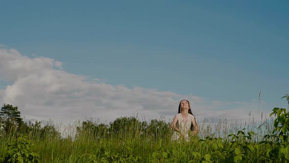 Happy School Age Girl in a White Dress Throws Up Wildflower Wreath and Jumping Against Background of