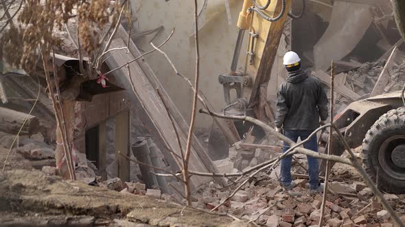 Engineer with Protective Helmet Looks at Demolition Destruction of Old Building Excavator Breaks