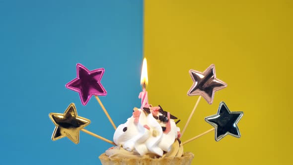 Birthday Cupcake with Candles and Birthday Decorations on a Blue and Yellow Background