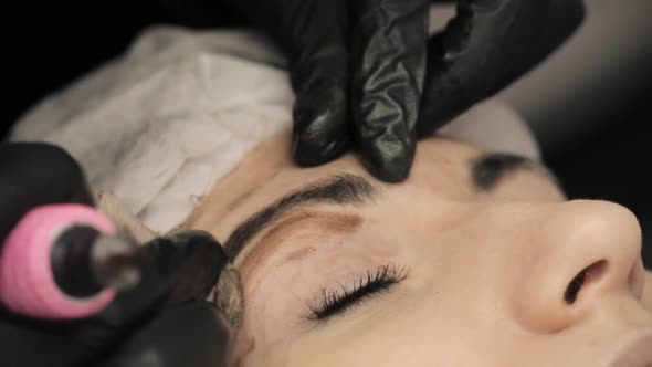 Close-up, the Hands of the Cosmetologist in Black Rubber Applying Permanent Make Up on Eyebrows-