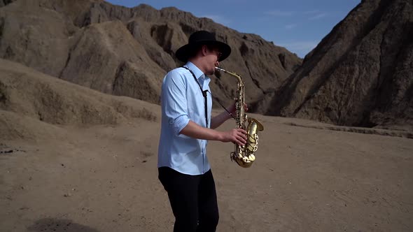 A Musician in a Hat Plays Jazz on a Saxophone Standing in the Desert Against the Background of Rocks